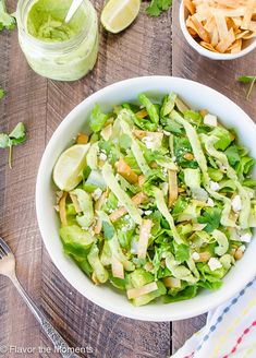 a white bowl filled with lettuce salad next to two small bowls of chips