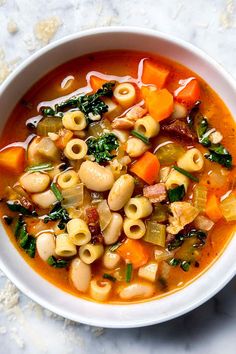 a bowl of pasta and vegetable soup on a marble countertop, with spoons to the side