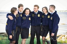 a group of young people standing next to each other near the water and grass in front of them