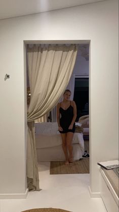 a woman in a black bathing suit is looking at herself through an open door to her bedroom