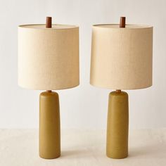 two lamps sitting next to each other on top of a white table with a beige lamp shade