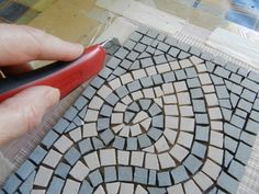 a person using a pair of scissors to cut out a mosaic tile design on the floor