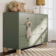 a baby's room with a green dresser and teddy bear