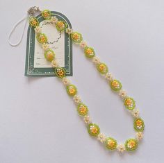 a green and yellow beaded necklace on a white surface with a tag attached to it