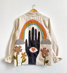 a white jacket with an image of a hand and flowers on it, hanging from a wooden hanger