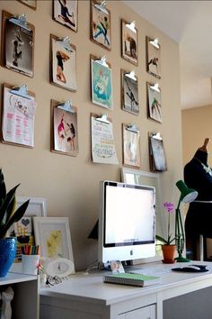 a desk with a computer on it in front of a wall full of pictures and photos