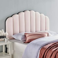 a pink headboard on top of a bed next to a night stand and nightstand