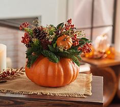 an orange pumpkin decorated with greenery and berries sits on a table next to a lit candle