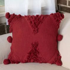 a red pillow with pom poms on it sitting on a white couch in front of a window