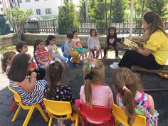 a woman sitting in front of a group of children on yellow chairs talking to each other