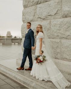 a bride and groom standing next to each other in front of a large stone wall