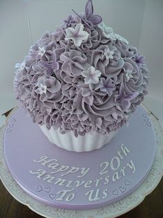 a cupcake decorated with purple flowers on top of a cake plate that says happy 20th anniversary to us