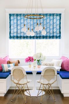 a dining room table with two chairs and a bench in front of a window covered by blue roman shades