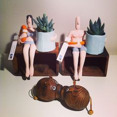 two figurines sitting on top of wooden boxes with plants in them and one holding a sign