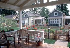 two wooden chairs sitting on top of a wooden deck next to flowers and houses in the background