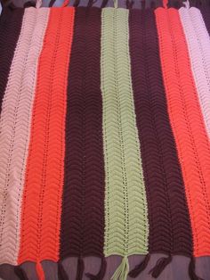 a crocheted blanket is laying on a bed with brown, green, and pink stripes