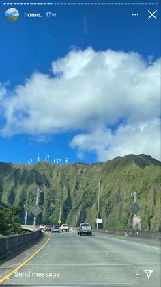 a car driving down the road with mountains in the back ground and clouds in the sky