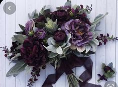 a bouquet of purple flowers and greenery on a white wooden background with ribbon tied around it