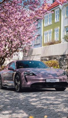 a pink sports car parked on the side of a road next to trees with purple flowers