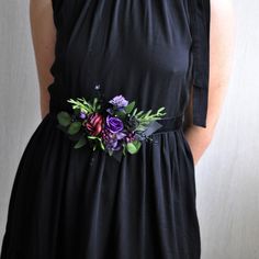 a woman wearing a black dress with purple and green flowers on the waist, in front of a white wall