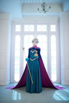 a woman in a blue and purple dress standing next to a chandelier holding a wand