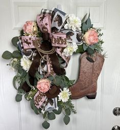 a wreath with flowers and cowboy boots hanging on the front door