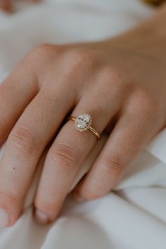 a woman's hand with a diamond ring on top of her finger and white sheets in the background