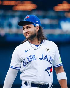 a baseball player with long hair wearing a white uniform and blue jays logo on his shirt