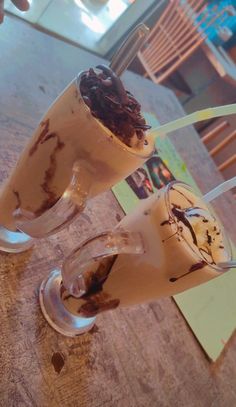 two glasses filled with ice cream and chocolate toppings on a wooden table in a restaurant