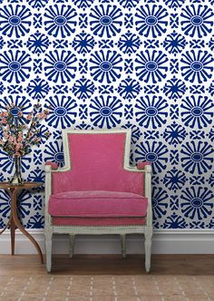 a pink chair sitting in front of a wall with blue and white designs on it