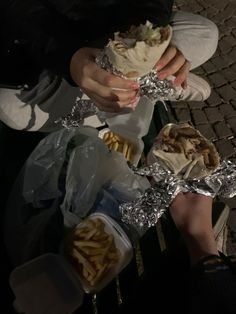 a person sitting on a bench with food wrapped around their hands and holding something in each hand