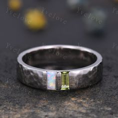 a white gold ring with a green tourmaline in the center on a stone surface