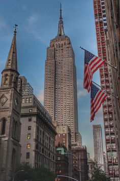 an american flag flying in front of the empire state building and other tall skyscrapers