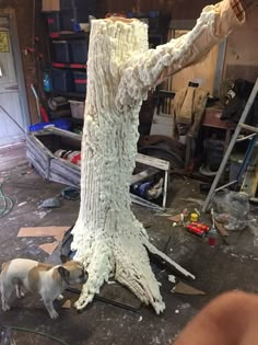 a dog standing next to a fake tree in a room filled with tools and other items