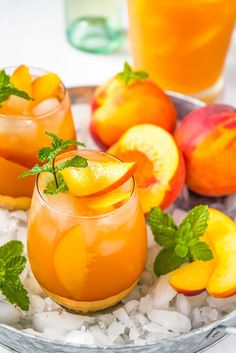 two glasses filled with orange juice and garnished with mint on ice next to sliced peaches