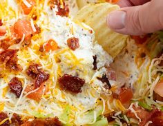 a hand holding a tortilla chip with bacon, cheese and lettuce