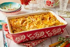 a red casserole dish filled with chicken and noodles on top of a wooden table