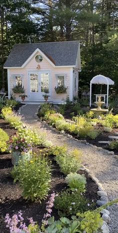 a white house surrounded by lots of trees and flowers in front of the house is a gravel path that leads to an outdoor seating area