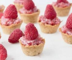 small raspberry tarts are arranged on a white surface