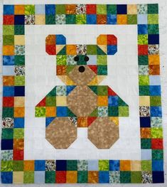 a teddy bear made out of patchwork on top of a white wall hanging quilt