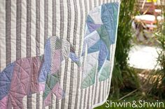 an elephant quilt hanging on the side of a bed in front of some trees and grass