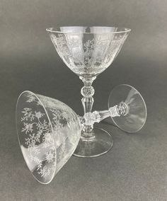 two glass goblets sitting next to each other on a gray tableclothed surface