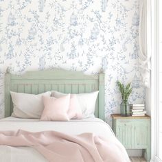 a bed with pillows and blankets on it in a bedroom next to a wallpapered wall