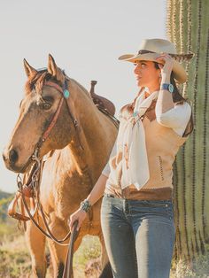 a woman in cowboy hat standing next to a brown horse near a saguado cactus