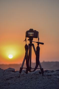 a tripod sitting on top of a sandy beach next to the ocean at sunset