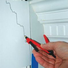 a hand holding some scissors in front of a piece of paper that is taped to the wall