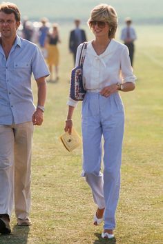 a man and woman walking in the grass with other people behind them on a sunny day