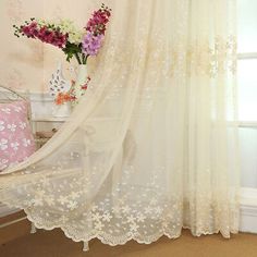 a white curtain with flowers on it in front of a bed and window sill