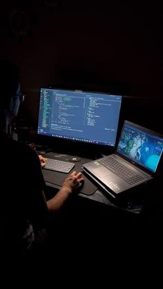 a man sitting at a desk with two laptops and a desktop computer in front of him