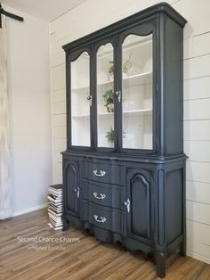 a black china cabinet with glass doors on the top and bottom, next to a stack of books